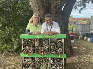 Two people standing behind a wooden bee house