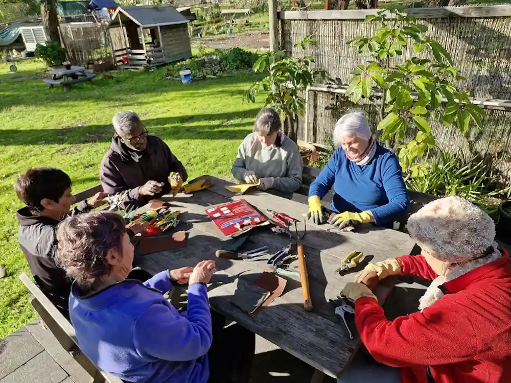 A group of people sitting at a table sharpening garden tools