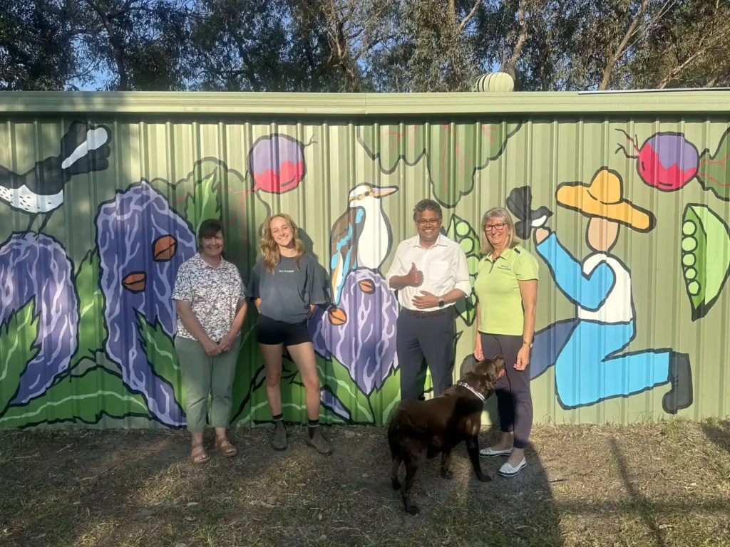 Four people standing in front of a garden shed with a painted mural